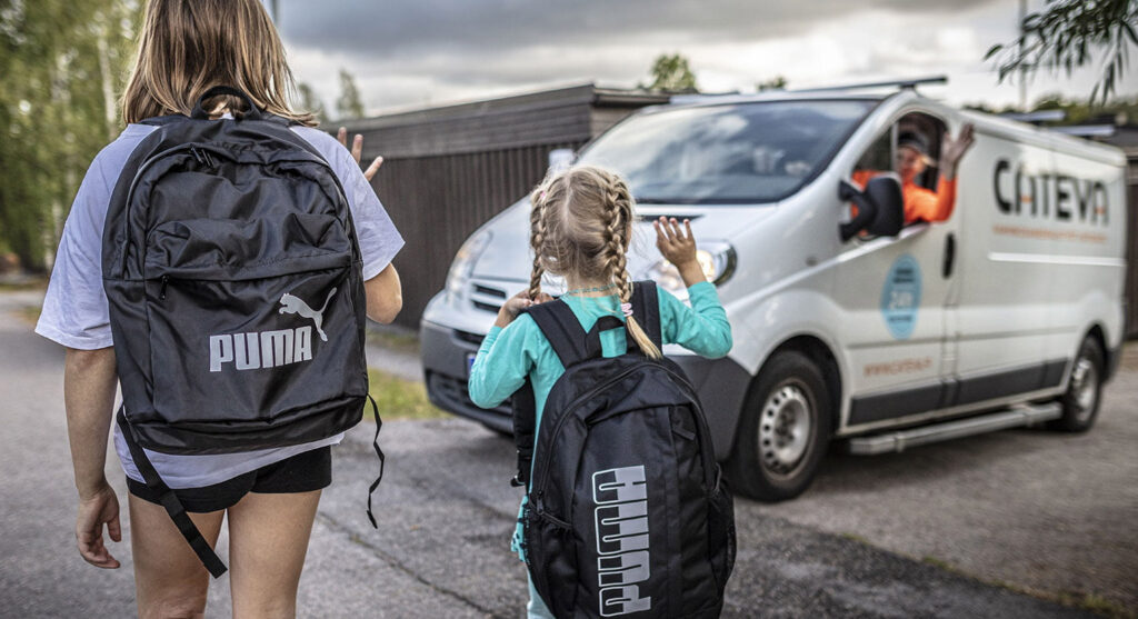 Kaksi koulutyttöä vilkuttavat pakettiautossa istuvalle Catevan työntekijälle